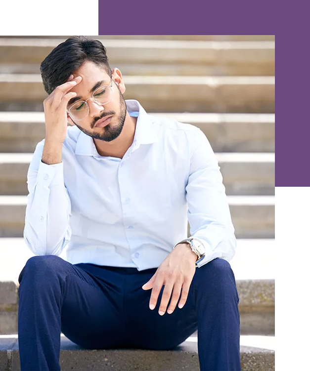 young man dressed in professional clothes sits with head in his hand, stressed with suicidal thoughts